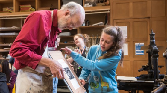 Two people look at a print in front of an old printing press