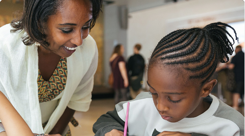 A woman watches a child draw