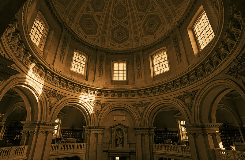 The circular interior of the Radcliffe Camera in low light, with sunlight falling from the windows