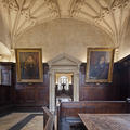Two paintings in gilt frames hanging on a panelled wall either side of a stone doorway